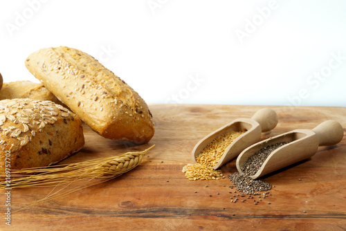 Rustic wooden board showcasing whole grain bread, wheat ear, and scoops of chia and flax seeds, promoting healthy eating