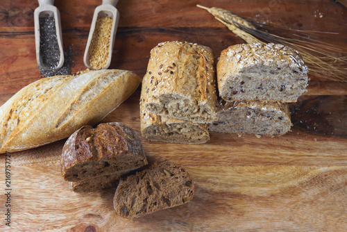 Bakery presenting different types of fresh whole grain bread, rolls, and a baguette with seeds on a rustic wooden background