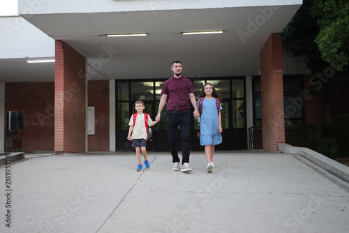 Back to school and education concept, father holding hands with his son and daughter walking from school building, family support.