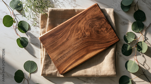 Photorealistic overhead flat lay of a rectangular rustic wooden cutting board with rich warm natural wood grain, centered diagonally on top of a folded beige linen kitchen cloth