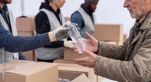 Close up view of a charity worker distributing a plastic bottle of clean drinking water to a grateful senior man outdoors.