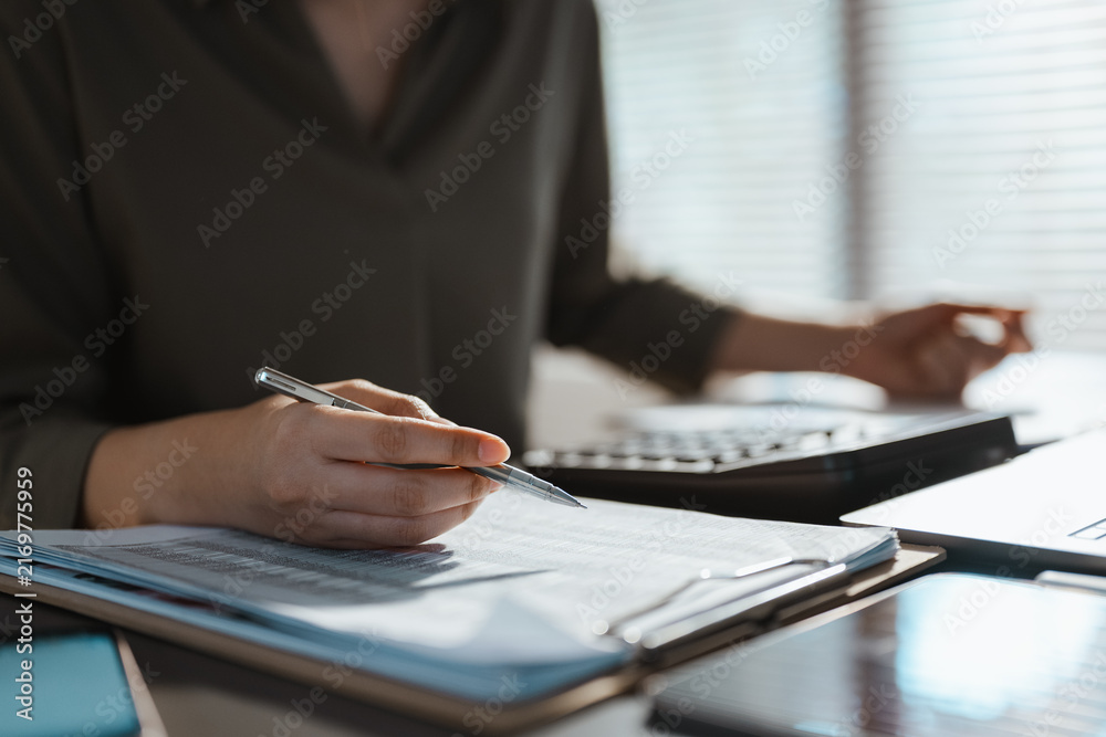Obraz premium An accountant writes on a budget report while checking a calculator, using financial analysis, planning, expense, revenue and variance review to turn budget figures into a practical forecast.