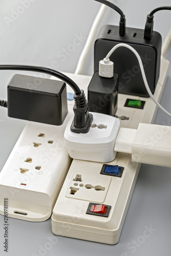 Close-up of overloaded electrical power strips with multiple plugs, adapters, and USB chargers connected in a risky daisy chain arrangement, illustrating electrical hazard concept