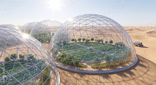 Large transparent geodesic greenhouse domes cultivating green crops and trees in arid desert sand dunes landscape under bright sun