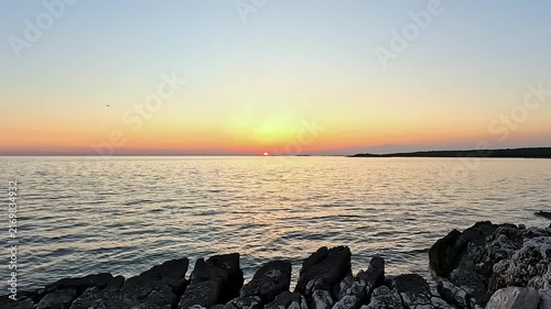 Sunset Over Calm Ocean Water and Rocky Shoreline with Glowing Horizon, Static