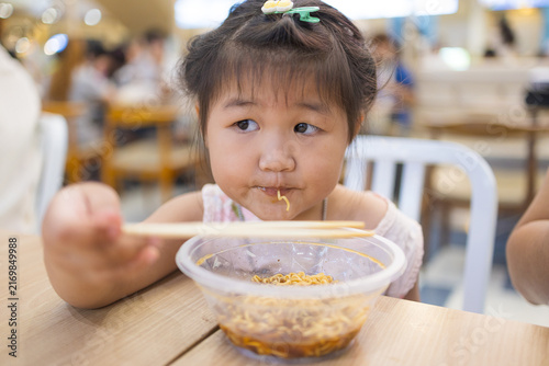 Canvastavla Cute Asian Girl Eating Instant Noodles with Chopsticks at a Restaurant,Close-up of an adorable little Asian girl enjoying a bowl of delicious instant noodles with chopsticks in a casual restaurant