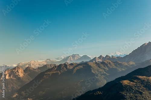 Fotografie Rolling Dolomite ridges recede into golden haze under a wide clear morning sky