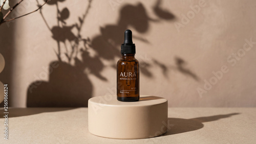 Amber glass dropper bottle of botanical serum placed on a cylindrical beige pedestal against a neutral textured background with soft shadows of plant leaves