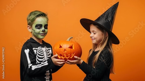 Children in halloween costumes holding a carved pumpkin