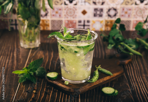 Cuadro en lienzo A refreshing cucumber peas mint drink in a glass with ice, surrounded by fresh herbs on a rustic wooden background