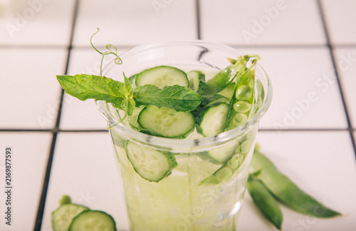 Fotografía A refreshing cucumber peas mint drink in a glass with ice, surrounded by fresh herbs on a rustic wooden background