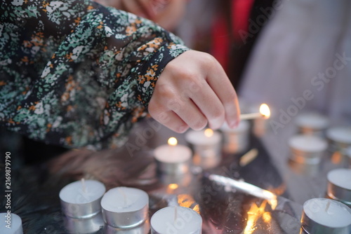 Quadro su tela A close-up of a woman’s hand striking a match to light tealight candles at a candlelight vigil, evoking remembrance, prayer, quiet reflection, hope and communal ritual