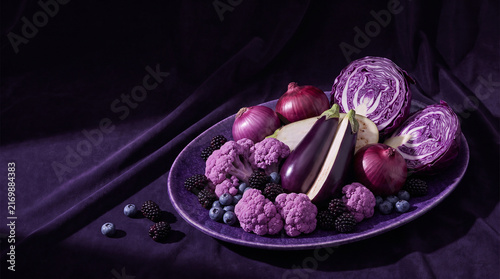 monochromatic food photography of purple vegetables and fruits including eggplant, purple cabbage, red onion, purple cauliflower, blackberries and blueberries arranged on a deep violet background 