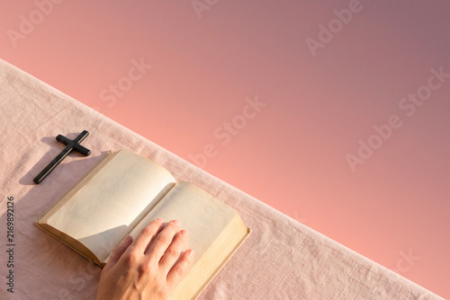 Person reading an open holy bible beside a wooden cross