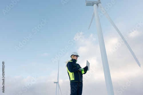 Woman engineer inspecting wind turbines in a snowy, cold environment with a laptop