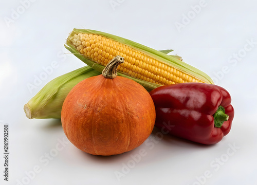 A collection of fresh autumn vegetables, including a ripe orange pumpkin, yellow corn cobs, and a vibrant red bell pepper, perfect for healthy food concepts.