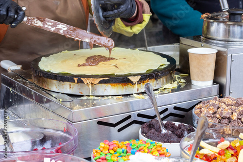 Pancakes are fried in a frying pan in the open air. Bowls of sweets nearby