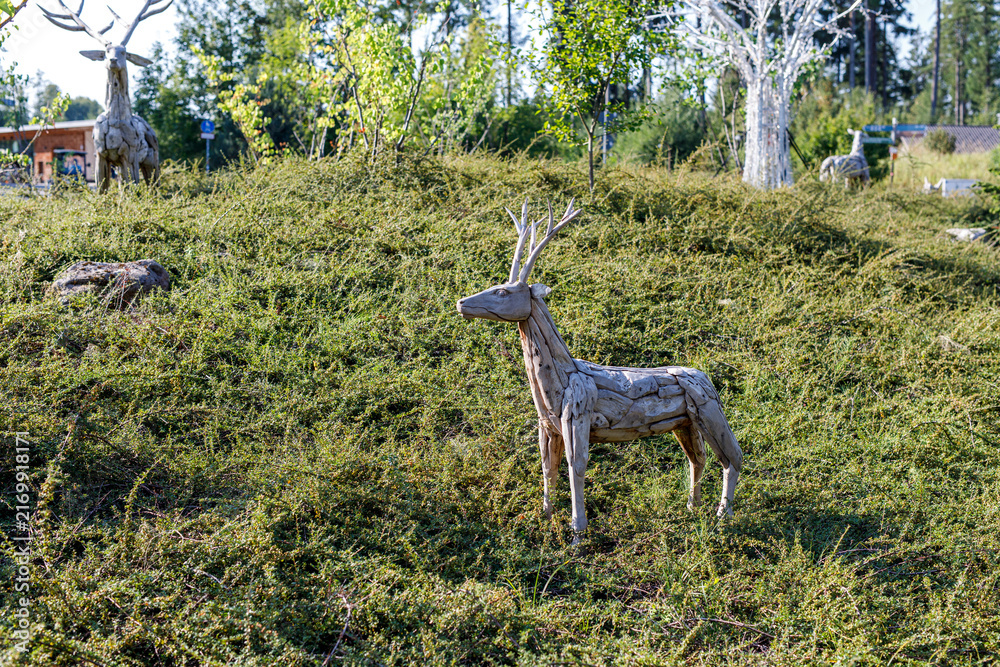 Naklejka premium Artistic driftwood deer sculpture standing on a lush green hill in a beautiful outdoor park setting.