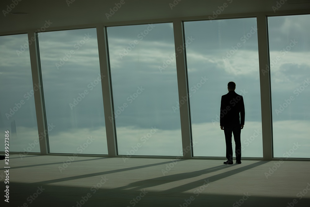 Fototapeta premium Man standing alone looking out large modern windows