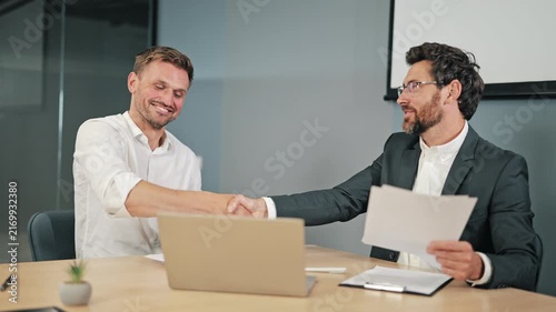 Two business professionals solidify deal with handshake in contemporary office setting. Important documents reviewed, marking successful collaboration and agreement between individuals agreement.