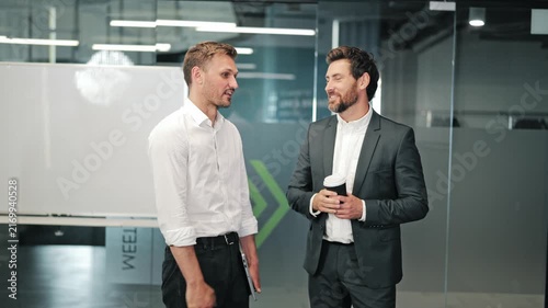 Professional men shake hands, engage in discussion. Conversation unfolds in contemporary office, featuring collaboration and shared ideas. Corporate interaction and successful communication shown.