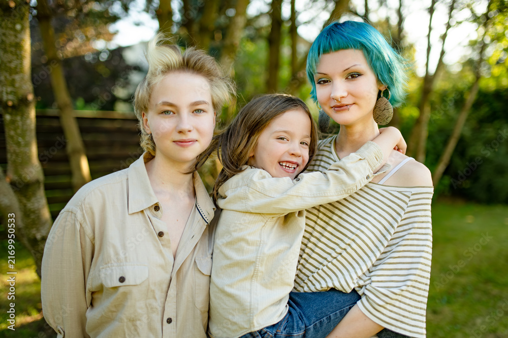 Fototapeta premium Three siblings pose together outdoors on a warm autumn day, with a smiling boy hugging his older sister. Natural family portrait in a garden setting.