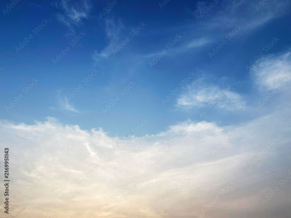 Obraz premium Serene blue sky with soft wispy white clouds illuminated by warm sunlight near the horizon