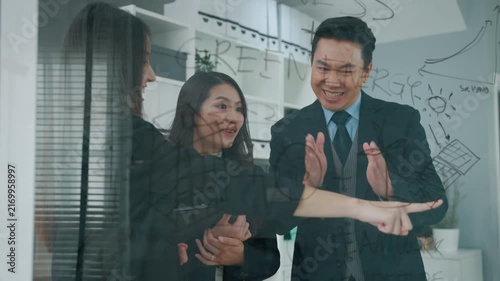 Business professionals reviewing a project plan and discussing strategy in a modern office. A female colleague points toward information on a transparent glass board while the team evaluates ideas tog