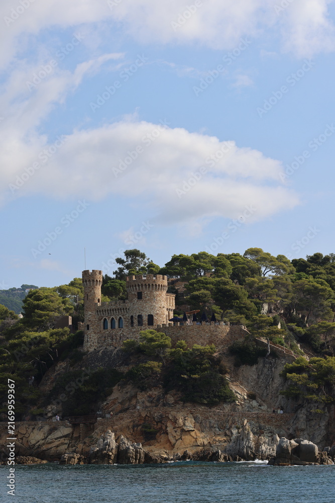Fototapeta premium Historic castle and fortified walls of Vila Vella in Tossa de Mar, Costa Brava, Spain. Scenic Mediterranean coastline with medieval architecture, rocky cliffs and lush pine trees overlooking the sea.