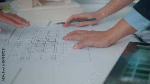 Close-up of professionals reviewing an architectural blueprint and marking building plans with a pencil on a modern office desk. The image represents architecture, engineering, construction planning a