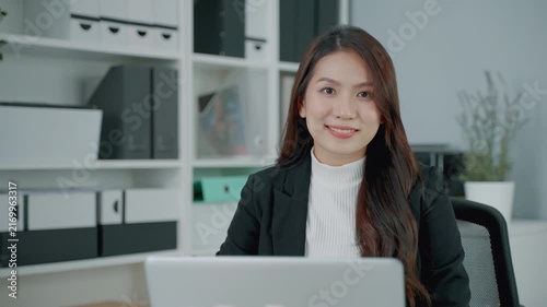 Confident professional woman working at a laptop in a modern office environment. The portrait represents business, career development, workplace technology, leadership, productivity and professional s