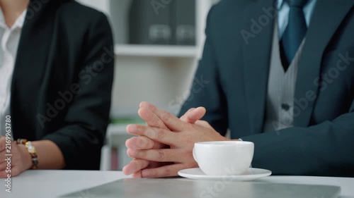 Close-up of business professionals engaged in a discussion during an office meeting. Hands and a coffee cup create a professional workplace scene representing communication, leadership, collaboration,