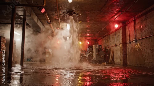 Water pouring from burst pipe in flooded basement with alarm lights