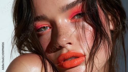 Studio head-and-shoulders portrait of a beautiful brunette with vibrant pink eye makeup and orange lips