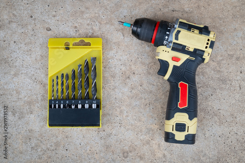 A set of drills of different diameters and an electric screwdriver against the background of concrete asphalt.