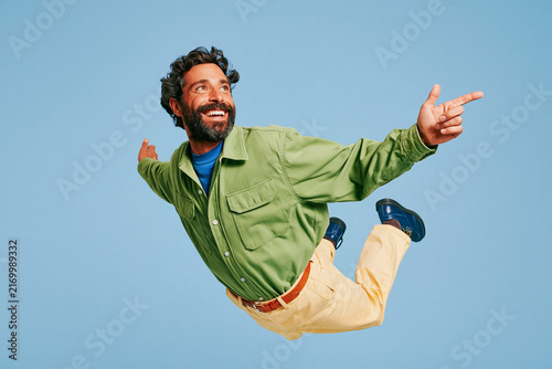 Playful Bearded Man Flying Against Blue Background