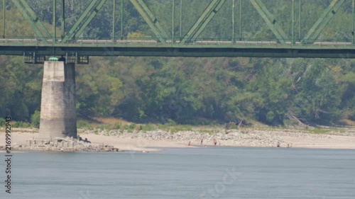 People swimming and relaxing on an exposed Danube riverbank beneath Medve bridge during extremely low summer water levels in Slovakia