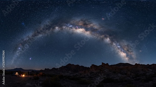 Bright milky way arch over camp fire and tent in desert landscape at night with clear stars for outdoor travel adventure.