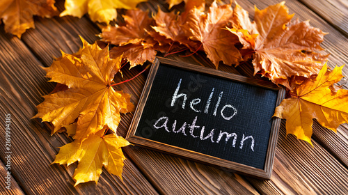 Hello autumn lettering written in white chalk on a small blackboard placed on a bright wooden background with an orange leaf frame arrangement autumn seasonal flat lay styling warm color