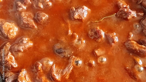 Slow cooking beef stew with rich gravy and bay leaf in a pan, close-up