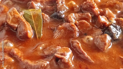 Slow cooking beef stew with rich gravy and bay leaf in a pan, close-up