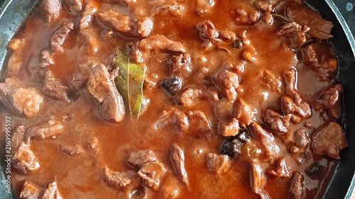 Slow cooking beef stew with rich gravy and bay leaf in a pan, close-up