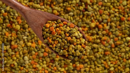 Bee pollen granules texture background with wooden spoon, close up. Top view of colorful pile of natural bee pollen granules with wooden spoon scoop full of grains used as superfood dietary supplement
