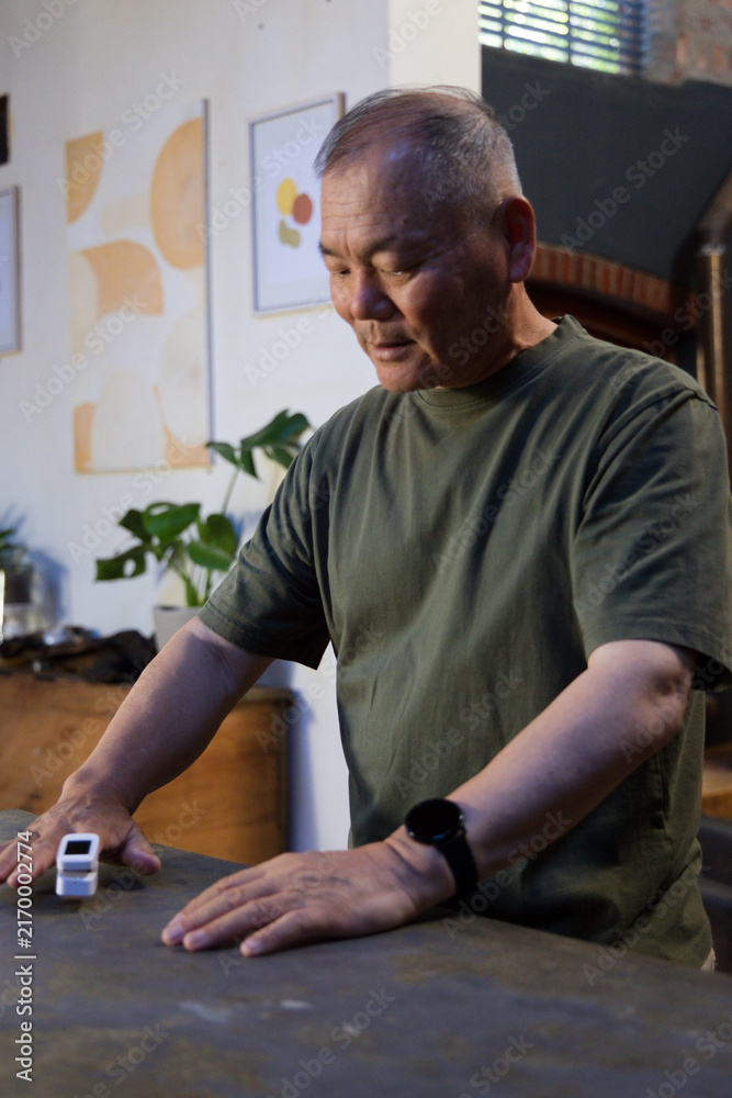 Fototapeta premium Senior Asian man wearing olive T-shirt and black wristwatch standing at home, gazing at toy car