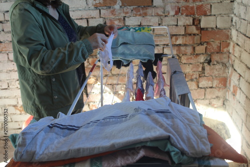 Woman Hanging Clothes on Drying Rack in Rustic Brick Interior.

