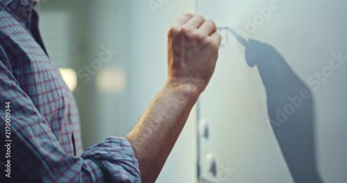 Man wearing a blue shirt writing the words “Education Online” on a whiteboard with a marker. Educational concept representing online learning, digital education, remote teaching, e-learning.