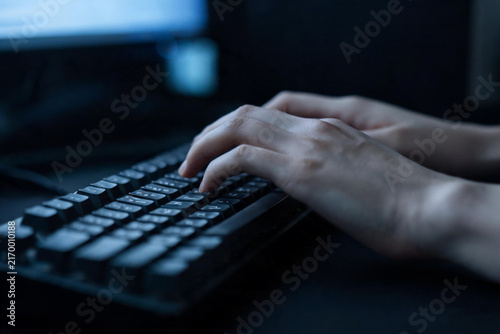 Close‑up of human hands typing on mechanical keyboard in dim dark office