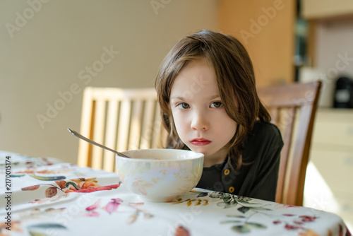Принти на полотні Young child sitting at a dining table and looking reluctant to eat his meal