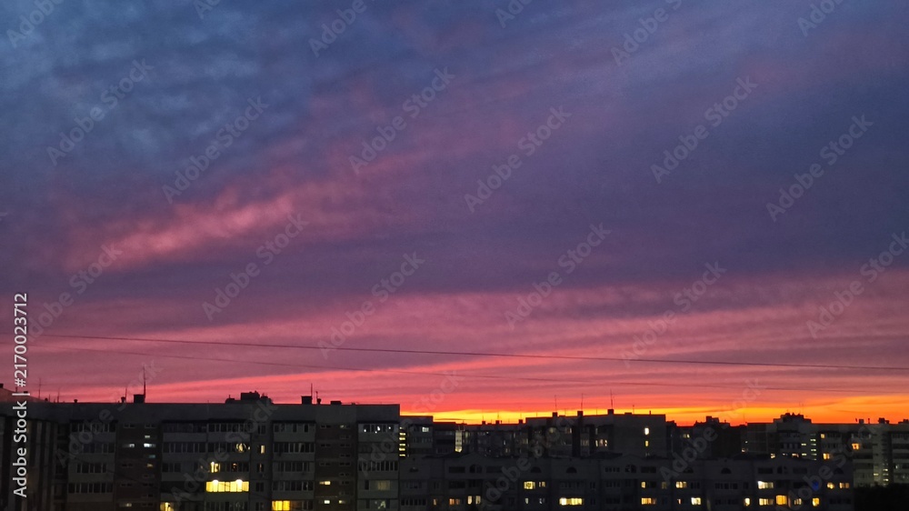 Fototapeta premium A bright red, orange, and blue sky over the city at sunset.
