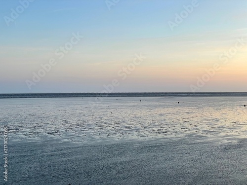 Die Sonne geht unter über dem Wattenmeer in Büsum an der deutschen Nordseeküste. Der Himmel über der Nordsee färbt sich diesem Sommertag orange und das Watt schimmert silbern.
